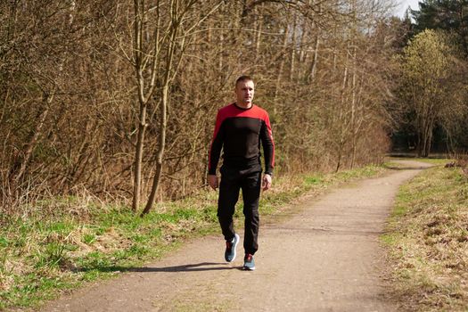Young male athlete in sportswear on a forest path. A man after a morning jog walks in the woods