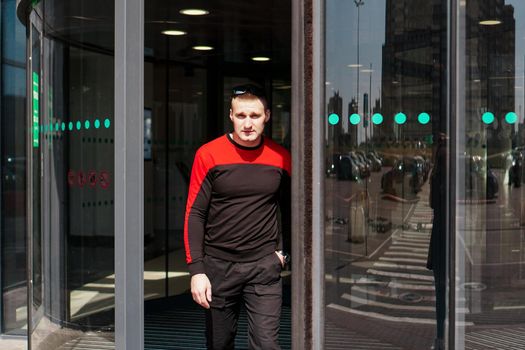 A young athletic man in a tracksuit walks out of the revolving doors of a hotel or shopping mall