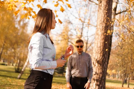 Unknown man in sunglasses watches a woman in autumn park