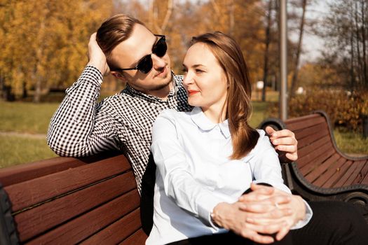 Happy smiling couple on park bench in fall sunny day