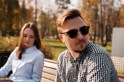 Young couple in quarrel sitting on bench in autumn park