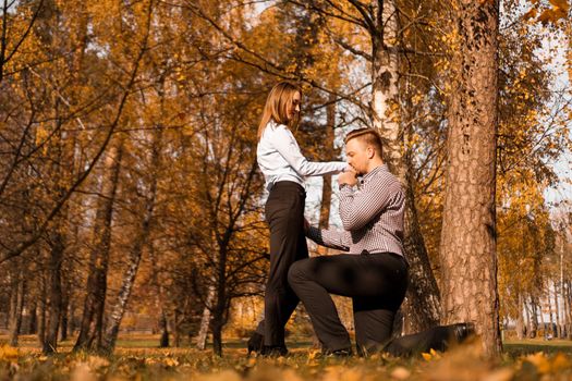 Love, couple, relationship and engagement concept - kneeled man kisses a hand a woman in the autumn park