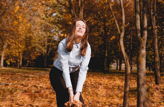 Woman throwing yellow leaves in the air - autumn park