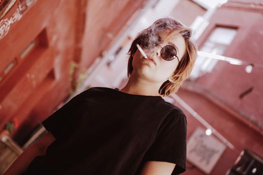 Millennial cool pretty girl with short red hair and mirror sunglasses smoking cigarette in the old city with red walls