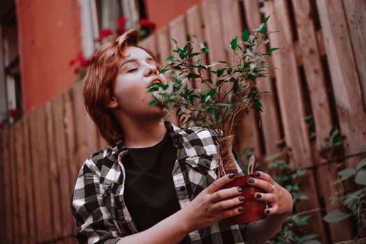 Young woman holds a flower in a pot, she grimaces and bites the flower in the backyard