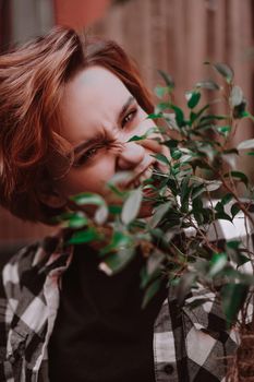 Young woman holds a flower in a pot, she grimaces and bites the flower in the backyard