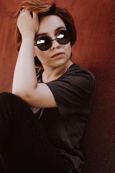 Portrait of attractive cheeky woman with short red hair in sunglasses at back yard in the old city with red walls