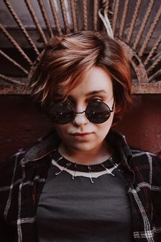 Portrait of attractive cheeky woman with short red hair in sunglasses at back yard in the old city with red walls