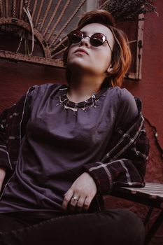 Portrait of attractive cheeky woman with short red hair in sunglasses at back yard in the old city with red walls