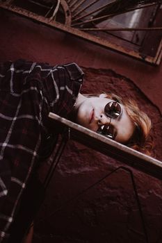 Portrait of woman with short red hair in sunglasses, head lies on table. Fatigue concept
