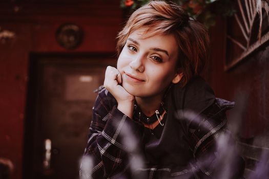 Outdoor portrait of young beautiful woman with short red hair posing with lavender flower. City lifestyle. Girl in the old city with red walls