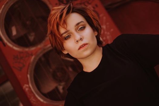 Portrait of attractive cheeky woman with short red hair at back yard in the old city with red walls