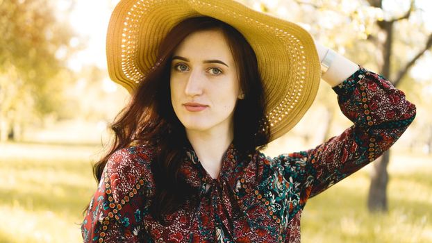 Summer portrait, beautiful young woman wearing straw hat at sunset time on the garden