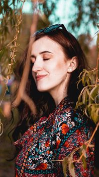 Beautiful young woman by branches with burgundy and green leaves. Romantic fashion look. Dreamy girl