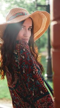 Portrait of pretty woman wearing dress and straw hat in sunny warm weather day. Walking at summer park.