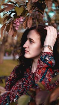 Beautiful young woman by branches with burgundy and green leaves. Romantic fashion look. Dreamy girl