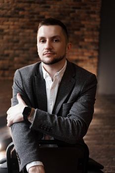 Portrait handsome fashionable man in a white shirt sits on a chair in a photo studio loft. Young businessman is thinking about future