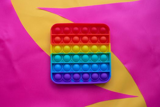 Pop it. A toy on a pink and yellow fabric background. Blue and Orange Funny Interactive Anti-Stress Silicone Toys.