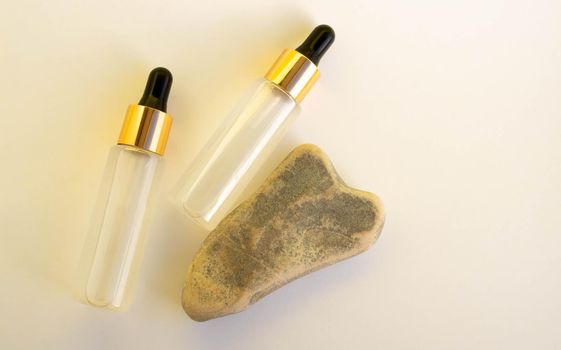 Two bottles of cosmetic liquid transparent gel next to a gray heart-shaped stone on a white background. Flat styling style.