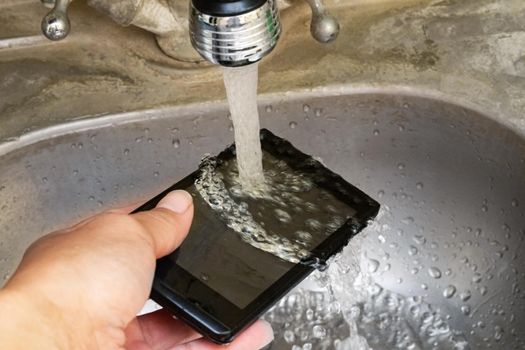 Touch mobile phone under tap water close up,