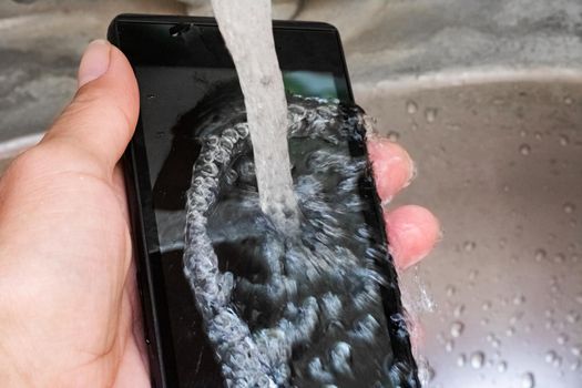 Touch mobile phone under tap water close up,