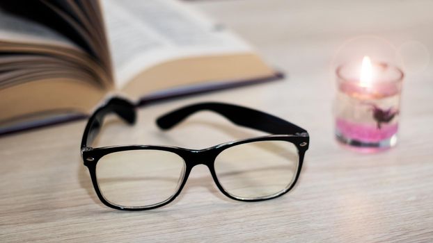 Bright candle and glasses in the dark on the background of the book close up