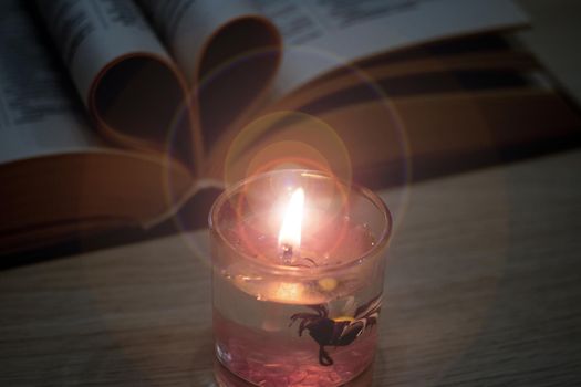 Bright candle in the dark against the background of the book close up