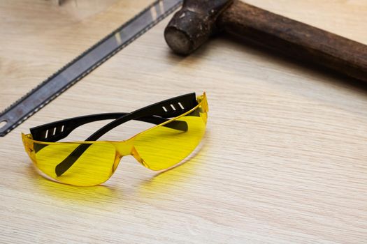 Yellow safety glasses and tools on wooden table close up