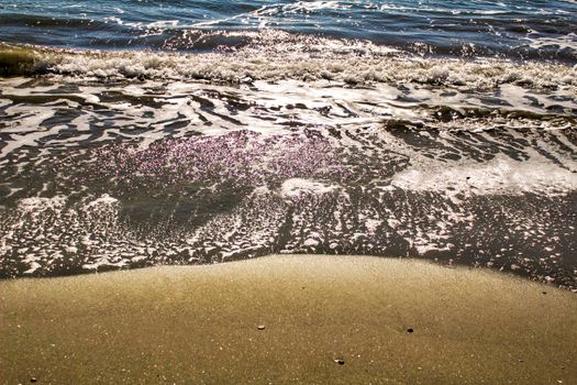 Waves, light and sand texture on the beach in the morning