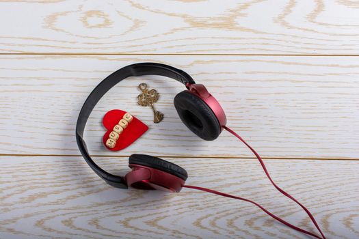 Red headphones, key and music written red heart  on a wooden background