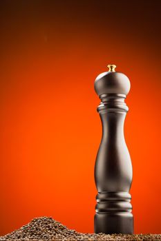 pepper mill and peppercorns heap, orange background