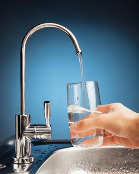 hand pouring a glass of water from filter tap, blue background