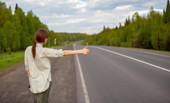 The girl stops the car on the highway with her hand. Stylish woman on the road stops the car go on a journey. A road in the middle of the forest.