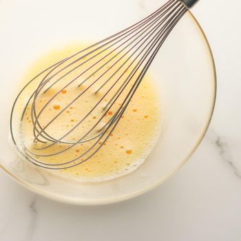 Cooking, meal and diet concept - Making of mixing eggs in bowl on marble table as homemade food flat lay, top view food brand photography flatlay and recipe for cooking blog, menu or cookbook design