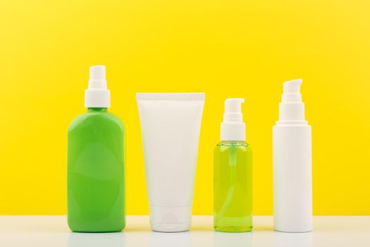 Set of green and white cosmetic bottles against yellow background. Concept of organic beauty products with natural ingredients or summer skin care products. Body spray, face cream, cleansing foam and exfoliating scrub