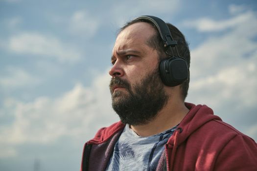 Middle-aged European man in headphones outdoors listening to music against the background of the sky