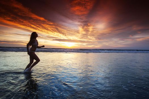 Woman running by the ocean beach at sunset