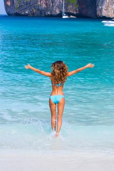 Carefree woman enjoying summer vacation in Thailand standing in water with arms raised