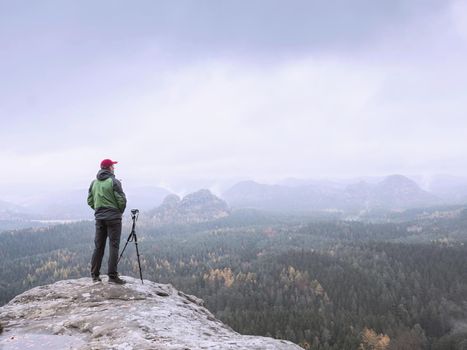 Alone man artist at tripod with camera thinking about composition. Misty mountains