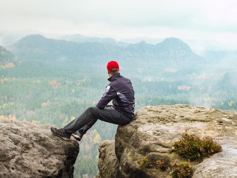 Sportsman relaxing at rocky edge in mountains, enjoy amazing view into morning hilly landscape