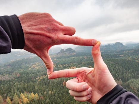 Man looking at hilly landscape framing with fingers, searching for image composition as he hiking over the mountain range. Landscape photographer 