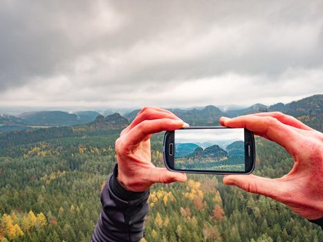 Man takes smart phone mobile photo on mountain landscape. Autumn season hike