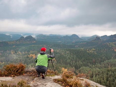 Alone man artist at tripod with camera thinking about composition. Misty mountains