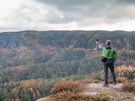 Man takes smart phone mobile photo on mountain landscape. Autumn season hike