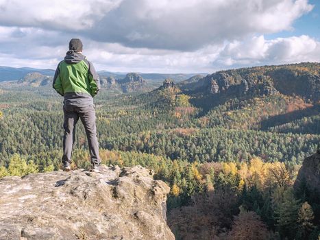 Single tourist on the edge of a mountain. Landscape covered with a lush carpet of colorful forests