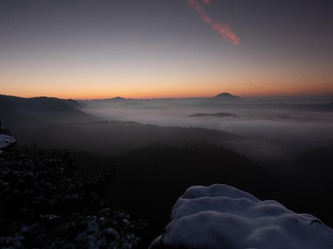 Chill morning with snow on rocky edge, valley full colorful mist. Winter hilly landscape 