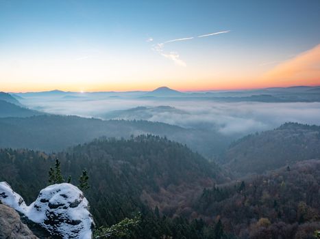 Chill morning with snow on rocky edge, valley full colorful mist. Winter hilly landscape 