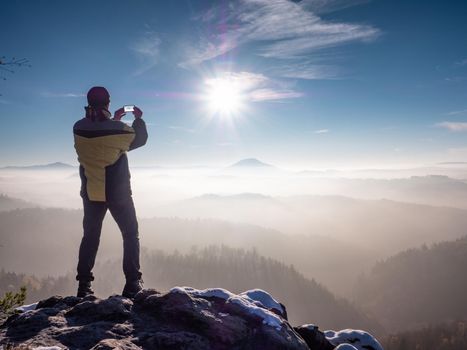 Man takes a photo on a mobile phone of a rocky ridge in winter morning. Beautiful landscape, hike, outdoor activities, tourism