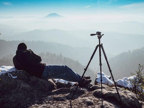 Photographer lays in snow shooting a picturesque winter landscape. Artist framing composition with camera in hands