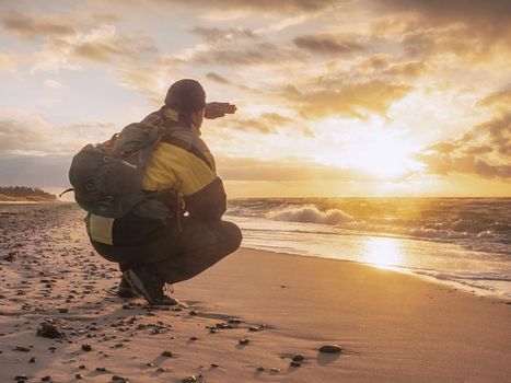 Man tourist  thinking and  meditates on the beach in the morning at sunrise. Relaxation and harmony. Man shadowing eyes
